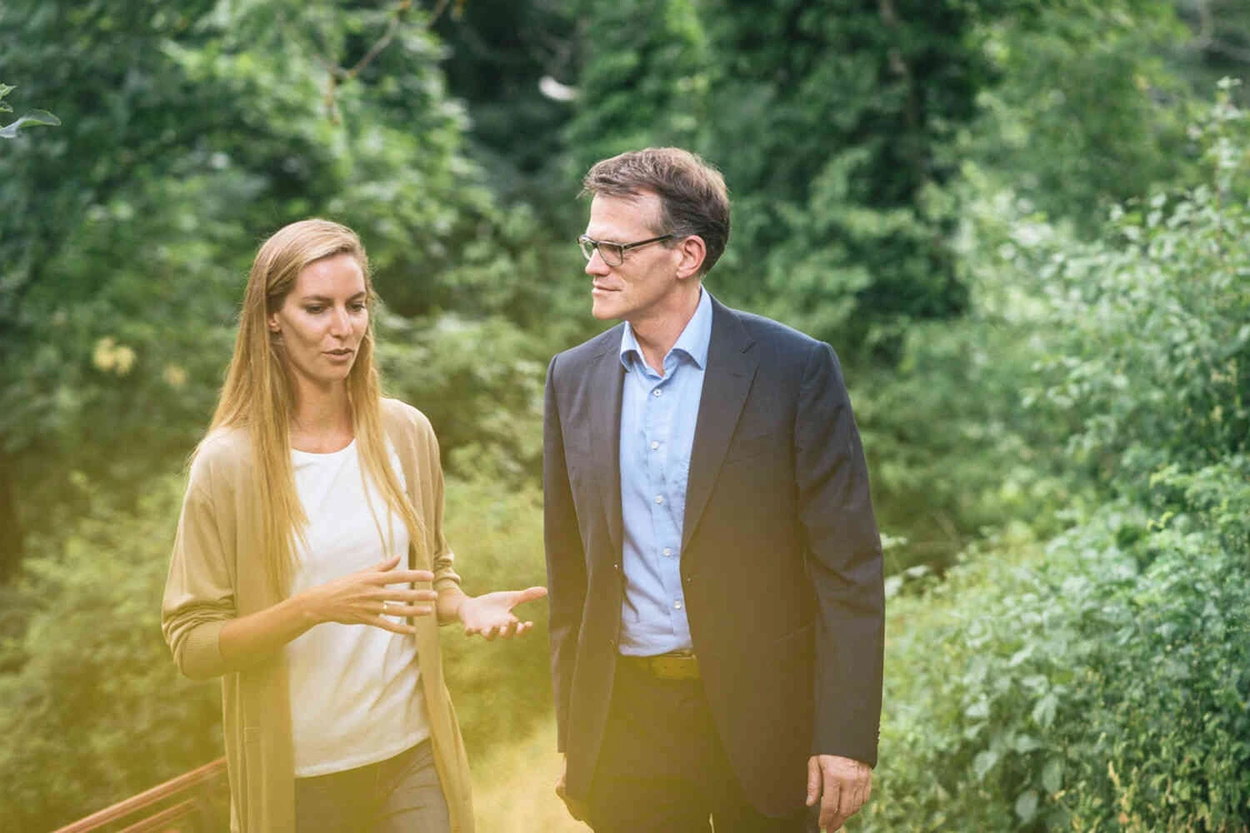 Therapeut und Patientin gehen im Garten und unterhalten sich.
